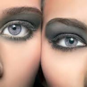 Puede incluir: Primer plano de dos ojos con un maquillaje de ojos ahumados dram&aacute;tico. Los ojos son de color azul claro y la sombra de ojos es de color gris oscuro.