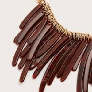 May include: A brown statement necklace with a gold chain and multiple long, thin, brown plastic pieces hanging from it.