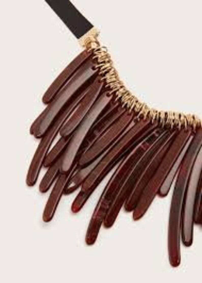 May include: A brown statement necklace with a gold chain and multiple long, thin, brown plastic pieces hanging from it.