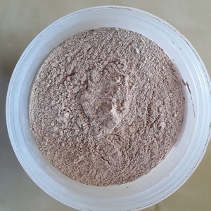 May include: A white plastic bowl filled with a light brown powder. The powder is smooth and fine, and it appears to be evenly distributed throughout the bowl.
