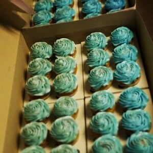 K&ouml;nnte beinhalten: Nahaufnahme einer Schachtel voller blauer und wei&szlig;er Cupcakes. Die Cupcakes sind in Reihen angeordnet und mit Frosting-Wirbeln verziert.