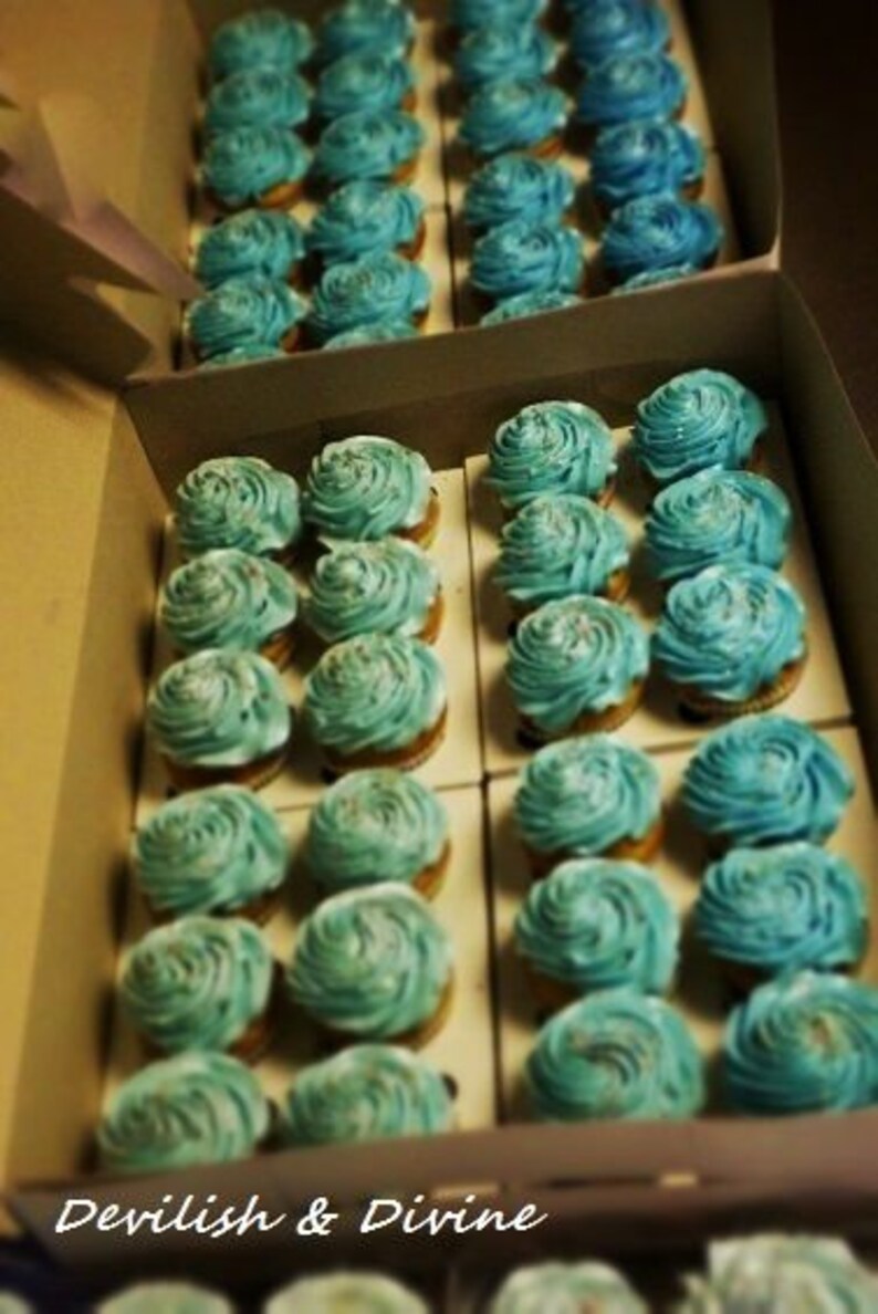 K&ouml;nnte beinhalten: Nahaufnahme einer Schachtel voller blauer und wei&szlig;er Cupcakes. Die Cupcakes sind in Reihen angeordnet und mit Frosting-Wirbeln verziert.