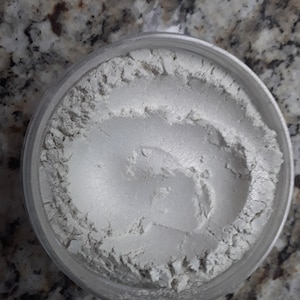 Puede incluir: Un pequeño frasco transparente lleno de polvo blanco iridiscente. El polvo es suave y tiene un ligero brillo.