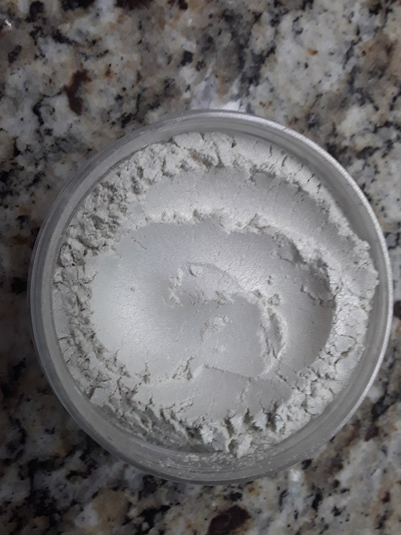 Peut inclure: Un petit pot transparent rempli de poudre blanche iris&eacute;e. La poudre est lisse et a un l&eacute;ger &eacute;clat.