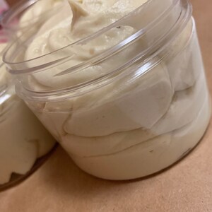 May include: A clear plastic jar filled with a thick, white cream. The cream is smooth and has a slightly textured surface.