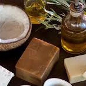 May include: A collection of natural beauty products including a half coconut shell, a bottle of oil, and four bars of soap. The soap bars are in various shades of brown and white.