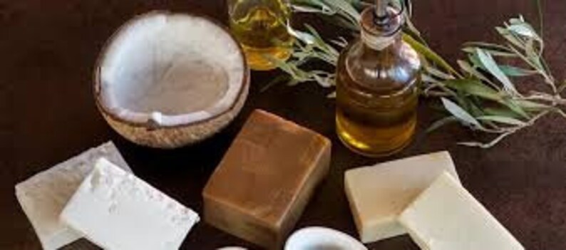 May include: A collection of natural beauty products including a half coconut shell, a bottle of oil, and four bars of soap. The soap bars are in various shades of brown and white.