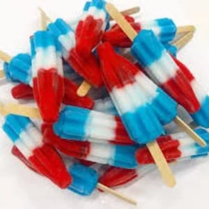 May include: A pile of red, white, and blue ice pops on wooden sticks. The frozen treats are arranged in a close-up shot, showcasing their vibrant colors and refreshing appearance. The popsicles are a classic summer treat.