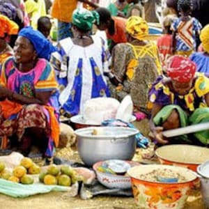 May include: A busy outdoor market with vendors selling fresh produce, grains, and other goods. The vendors are wearing colourful clothing and head coverings, creating a vibrant atmosphere.