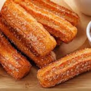 May include: A close-up of a plate of churros, a traditional Spanish dessert, with two dipping sauces: chocolate and caramel. The churros are golden brown and dusted with sugar.