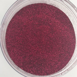 Könnte beinhalten: Ein transparentes Plastikgefäß gefüllt mit feinem, glitzerndem, burgunderrotem Glitter.