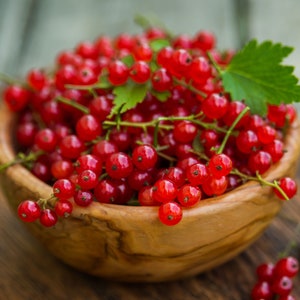 May include: A wooden bowl filled with bright red currants. The bowl is on a wooden surface.