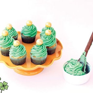 K&ouml;nnte beinhalten: Sechs gr&uuml;ne Cupcakes mit goldenen Streuseln und gr&uuml;nem Frosting auf einem gelben Kuchenst&auml;nder. Eine Sch&uuml;ssel mit gr&uuml;nem Frosting steht auf dem Tisch neben dem St&auml;nder.