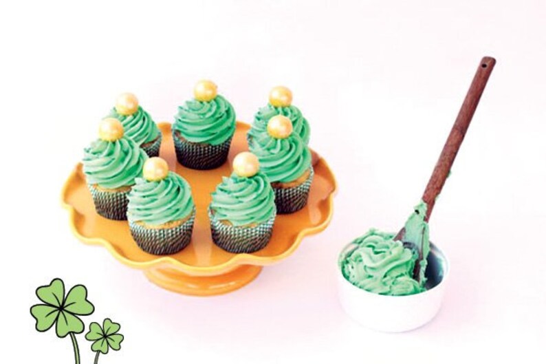 K&ouml;nnte beinhalten: Sechs gr&uuml;ne Cupcakes mit goldenen Streuseln und gr&uuml;nem Frosting auf einem gelben Kuchenst&auml;nder. Eine Sch&uuml;ssel mit gr&uuml;nem Frosting steht auf dem Tisch neben dem St&auml;nder.