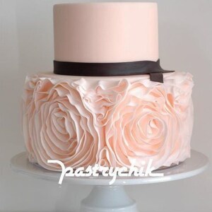 Peut inclure: Un g&acirc;teau de mariage &agrave; deux &eacute;tages avec un gla&ccedil;age rose p&acirc;le et un ruban noir. L'&eacute;tage inf&eacute;rieur est d&eacute;cor&eacute; d'un motif pliss&eacute;.