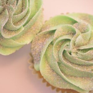 K&ouml;nnte beinhalten: Zwei gr&uuml;ne Cupcakes mit glitzerndem Frosting. Das Frosting ist spiralf&ouml;rmig und hat eine hellgr&uuml;ne Farbe mit silbernem Glitter.