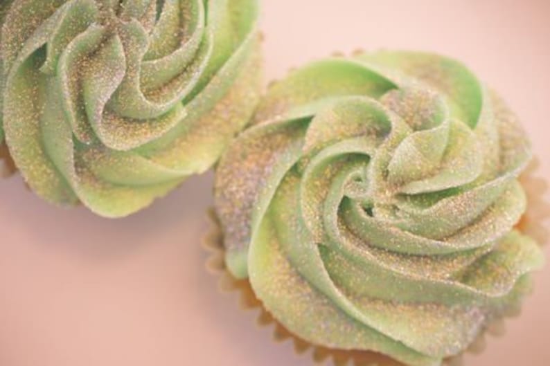 K&ouml;nnte beinhalten: Zwei gr&uuml;ne Cupcakes mit glitzerndem Frosting. Das Frosting ist spiralf&ouml;rmig und hat eine hellgr&uuml;ne Farbe mit silbernem Glitter.