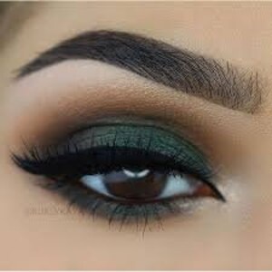 May include: Close-up of a green eyeshadow look with a winged eyeliner. The eyeshadow is a dark green with a shimmery finish. The eyeliner is black and creates a sharp wing.