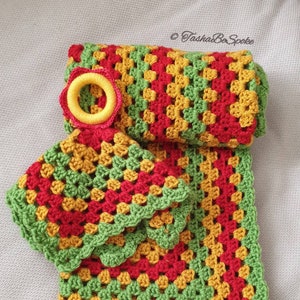 May include: A handmade crochet set in a granny square pattern. The set includes a folded blanket, a potholder, and a decorative ring. The colors are red, yellow, and green, with a green scalloped border. The set is likely for kitchen use.