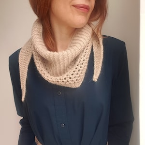 Puede incluir: Una bufanda de ganchillo beige con un delicado patr&oacute;n de calado. La bufanda se lleva alrededor del cuello de una persona que lleva un vestido camisa azul oscuro con un cintur&oacute;n de piel de serpiente.