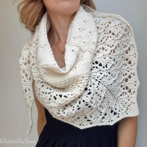 May include: A white crocheted shawl with a delicate lace pattern. The shawl is draped around a person's shoulders and neck.