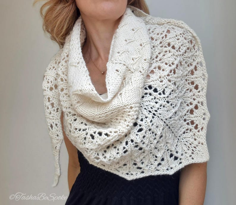 May include: A white crocheted shawl with a delicate lace pattern. The shawl is draped around a person's shoulders and neck.