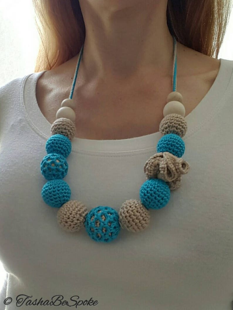 Op de afbeelding: Een handgemaakte ketting met gehaakte en houten kralen. De ketting heeft afwisselend lichtblauwe en beige gehaakte kralen, met natuurlijke houten kralen. De ketting is geregen op een blauw-wit koord.