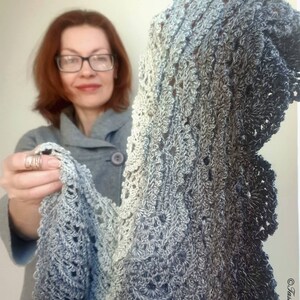 May include: A grey and white crocheted shawl with a scalloped edge. The shawl is made with a gradient yarn that transitions from light grey to dark grey.