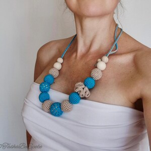Op de afbeelding: Een handgemaakte ketting met blauwe, beige en houten kralen. De ketting heeft een blauw koord en een haakontwerp. De kralen vari&euml;ren in grootte en textuur, waardoor een visueel aantrekkelijk accessoire ontstaat. Een uniek sieraad.