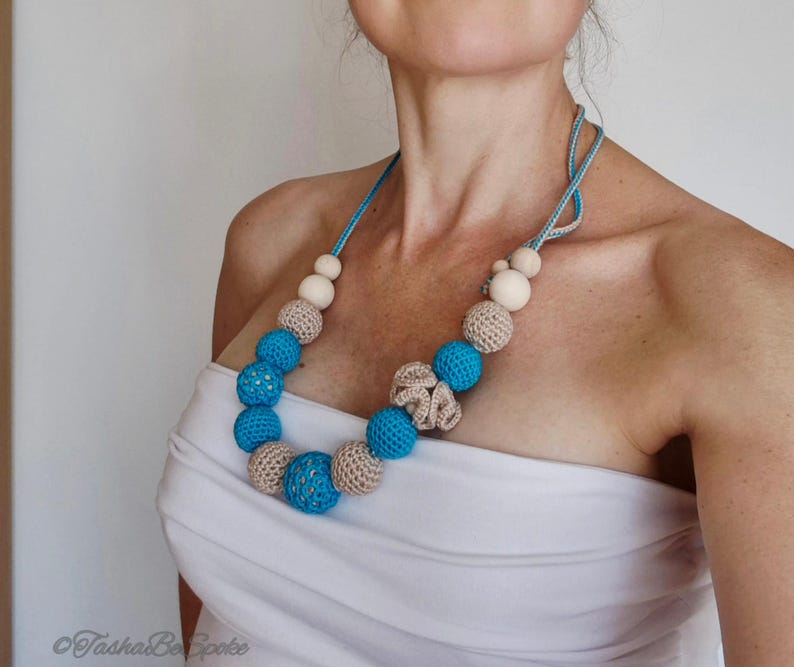 Op de afbeelding: Een handgemaakte ketting met blauwe, beige en houten kralen. De ketting heeft een blauw koord en een haakontwerp. De kralen vari&euml;ren in grootte en textuur, waardoor een visueel aantrekkelijk accessoire ontstaat. Een uniek sieraad.