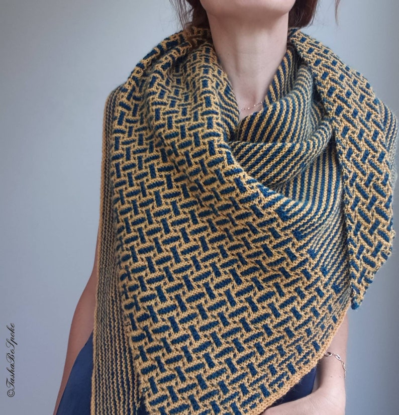 Pode incluir: Um xale de malha amarelo e azul com um padr&atilde;o geom&eacute;trico. O xale est&aacute; drapeado em volta do pesco&ccedil;o e dos ombros de uma pessoa.