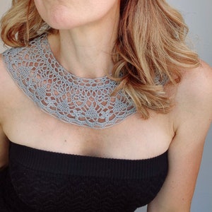 May include: A gray crocheted collar necklace with a delicate, intricate pattern. The collar is worn by a person with long blonde hair.