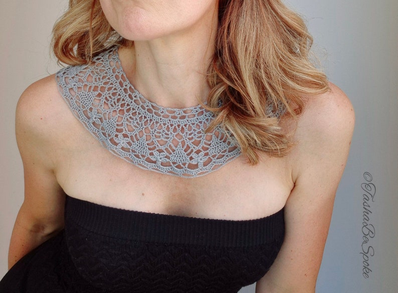May include: A gray crocheted collar necklace with a delicate, intricate pattern. The collar is worn by a person with long blonde hair.