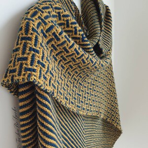 Pode incluir: Uma echarpe de malha com um padr&atilde;o geom&eacute;trico de amarelo mostarda e azul turquesa. A echarpe est&aacute; drapeada sobre um ramo de madeira.