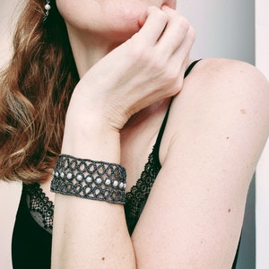 Puede incluir: Un brazalete negro y blanco con cuentas y un delicado patr&oacute;n de encaje. El brazalete se lleva en la mu&ntilde;eca.