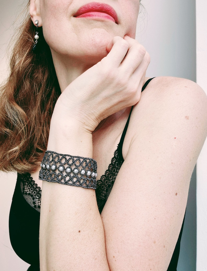 Puede incluir: Un brazalete negro y blanco con cuentas y un delicado patr&oacute;n de encaje. El brazalete se lleva en la mu&ntilde;eca.
