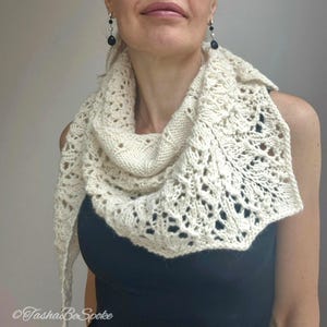 May include: A white crocheted shawl with a delicate lace pattern. The shawl is draped around the neck of a person wearing a black top.