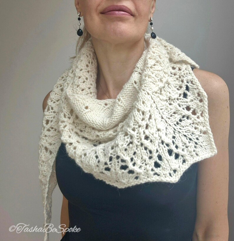 May include: A white crocheted shawl with a delicate lace pattern. The shawl is draped around the neck of a person wearing a black top.