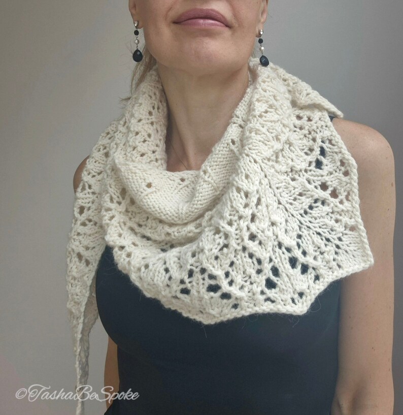 May include: A white crocheted shawl with a delicate lace pattern. The shawl is draped around a person's neck and shoulders.