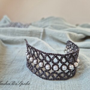 Puede incluir: Un brazalete de encaje negro con un dise&ntilde;o delicado y detalles de perlas blancas.