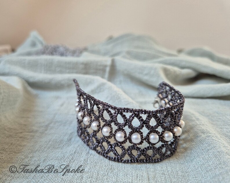 Puede incluir: Un brazalete de encaje negro con un dise&ntilde;o delicado y detalles de perlas blancas.