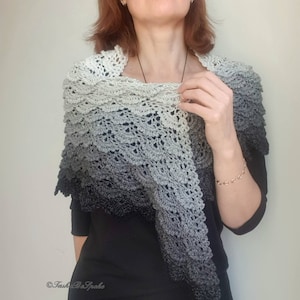 May include: A grey and black ombre crochet shawl with a delicate lace pattern. The shawl is draped over the shoulders of a person wearing a black shirt.