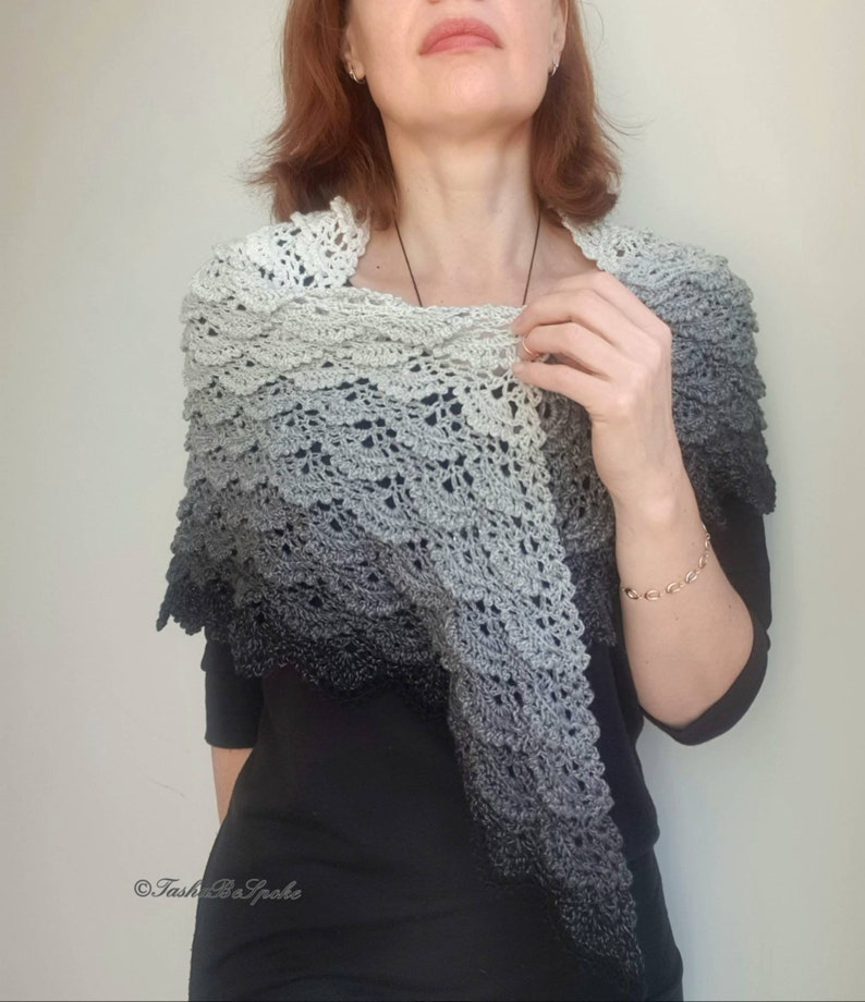 May include: A grey and black ombre crochet shawl with a delicate lace pattern. The shawl is draped over the shoulders of a person wearing a black shirt.
