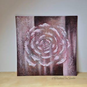 May include: A square canvas artwork depicting a textured rose in relief, in shades of pink and white. The background features vertical stripes of brown and pink. The artist's signature, "TashaBeSpoke", is visible in the lower right corner.
