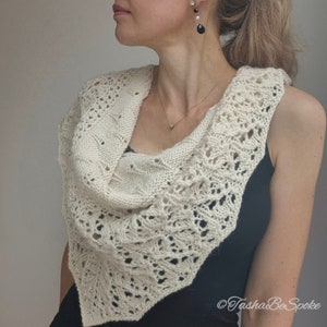 May include: A white crocheted shawl with a delicate lace pattern. The shawl is draped around the shoulders of a person wearing a black sleeveless top.