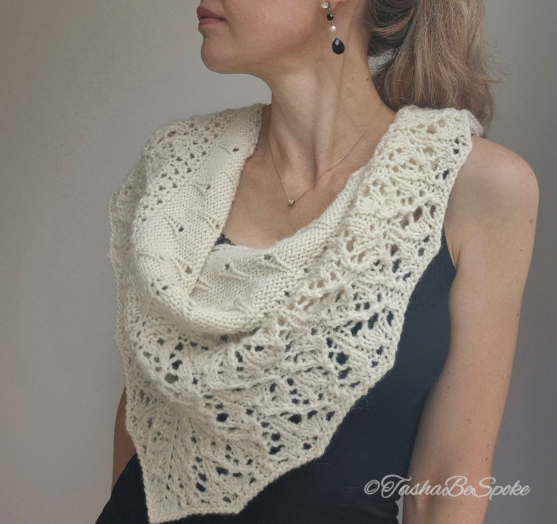 May include: A white crocheted shawl with a delicate lace pattern. The shawl is draped around the shoulders of a person wearing a black sleeveless top.