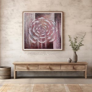 May include: An abstract painting of a rose in pink and white tones is framed and displayed above a wooden console table. The artwork has textured brushstrokes, creating a 3D effect. The room has a neutral colour palette with a vase of greenery.