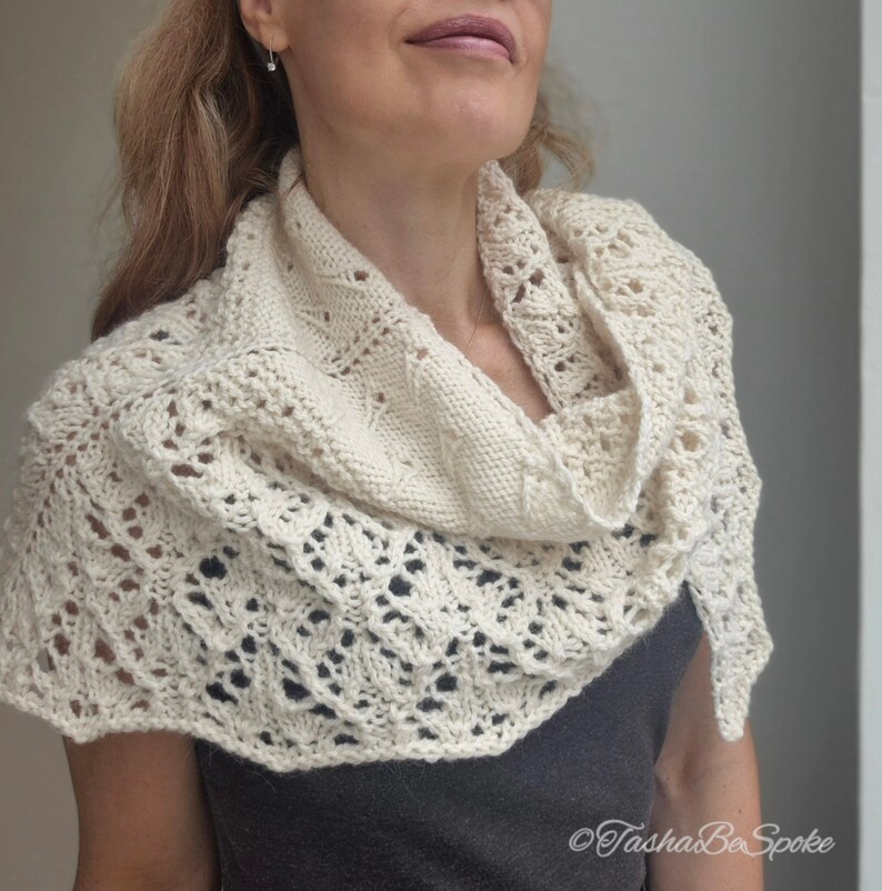 May include: A white crocheted shawl with a delicate lace pattern. The shawl is draped around a person's neck and shoulders.