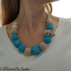Op de afbeelding: Een handgemaakte ketting met een verscheidenheid aan kralen. De ketting bevat lichtblauwe gehaakte kralen, beige gehaakte kralen en natuurlijke houten kralen. De ketting is geregen op een lichtblauw koord.