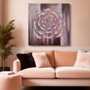 May include: A textured painting of a white rose on a canvas with a striped background of burgundy and cream. The artwork hangs above a peach-coloured sofa with decorative cushions. The room has a warm, inviting atmosphere.